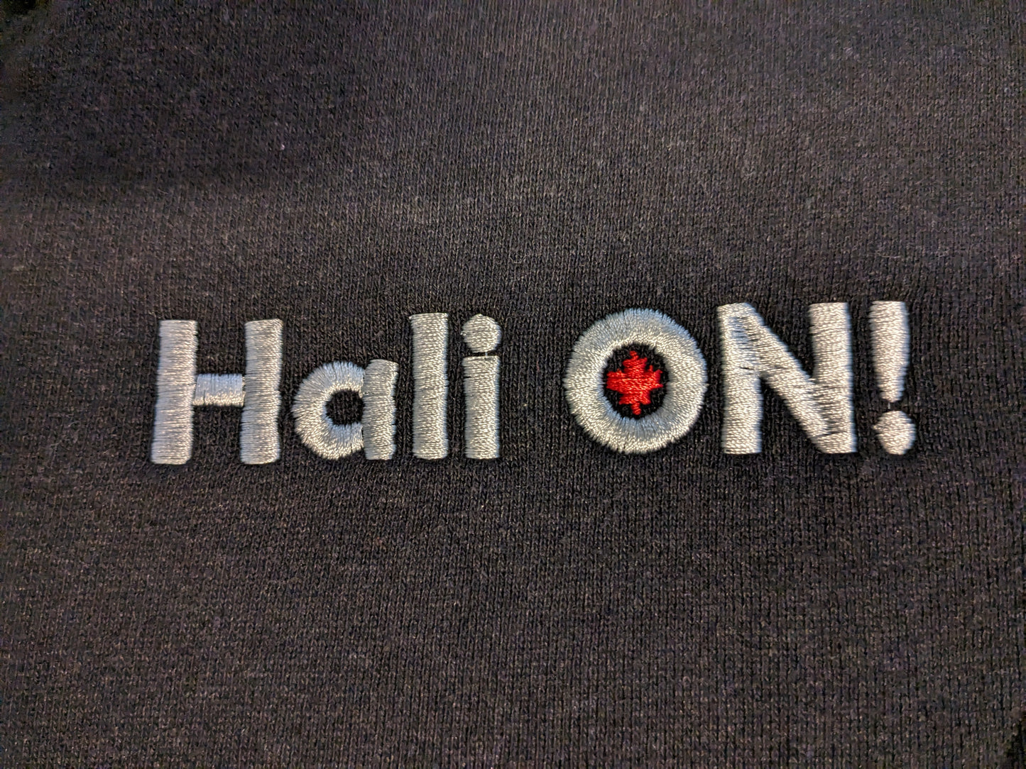 HALI ON! Hemp Fleece Track Jacket- Men's sizing (this is a close up of the HALI ON! embroidery in light grey with red maple leaf inside the 'O')
