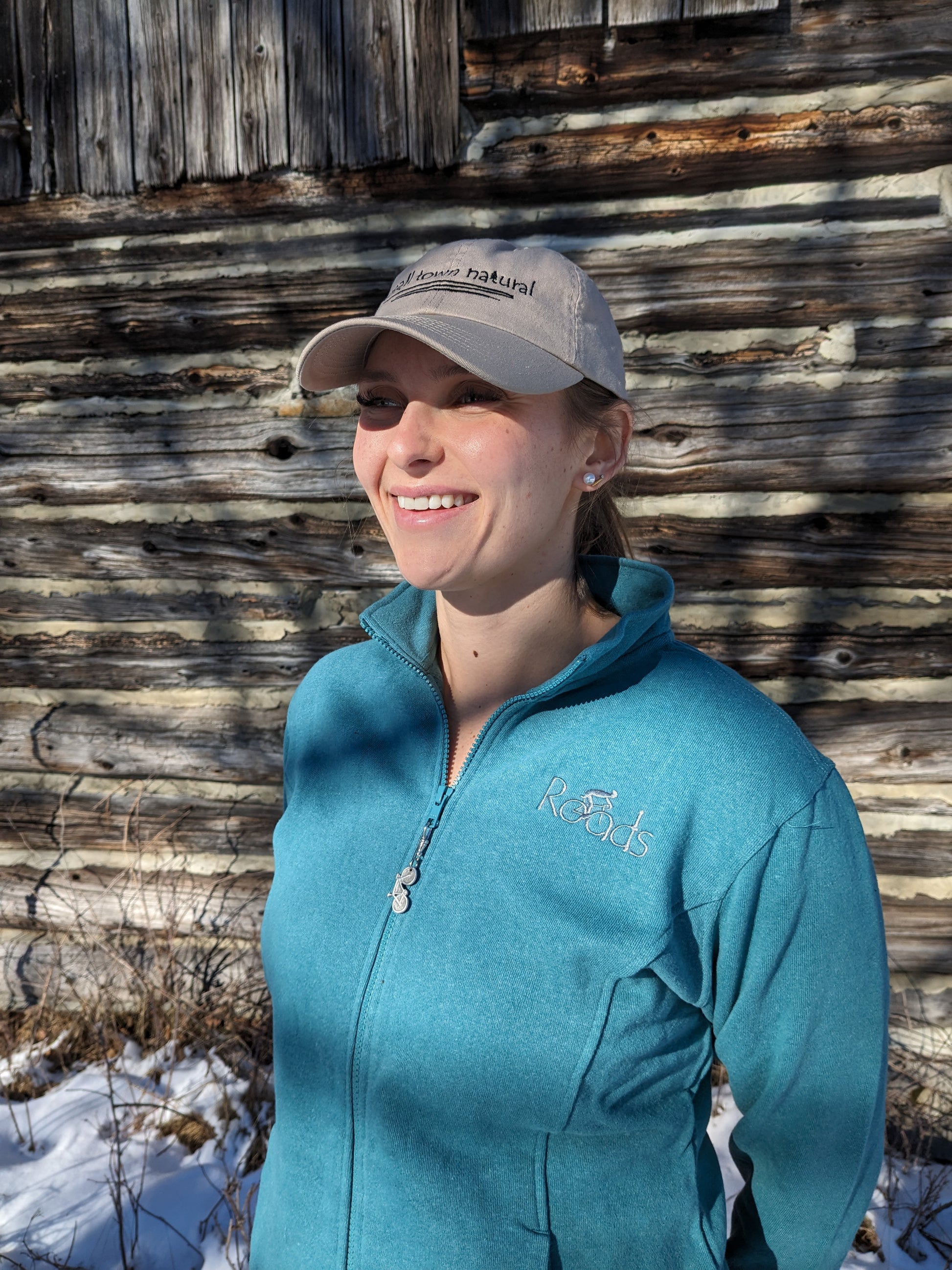 Our model Morgan is wearing teal track jacket with 'Roads' embroidered on upper left chest.'Roads' is another original design from Small Town Natural. This design is a tribute to Road and Gravel Road cyclists. Each jacket includes a removable bicycle zipper pull made of Pewter hand made in the small town of Tweed, Ontario.